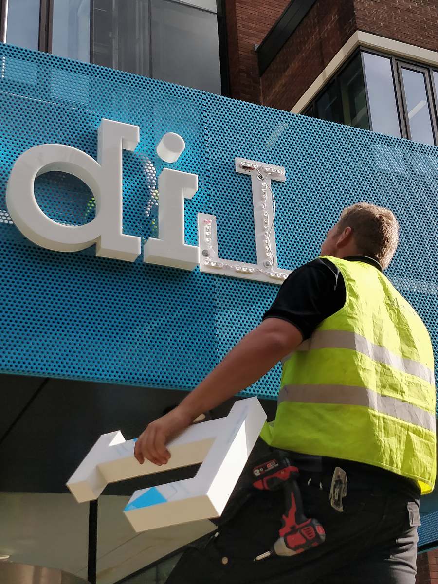 person person wearing yellow reflector vest in front of blue and white sign panel word