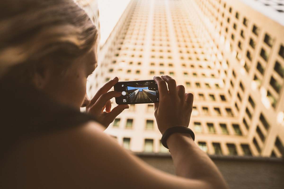 person selective focus photography of woman taking low angle photo of high-rise building people