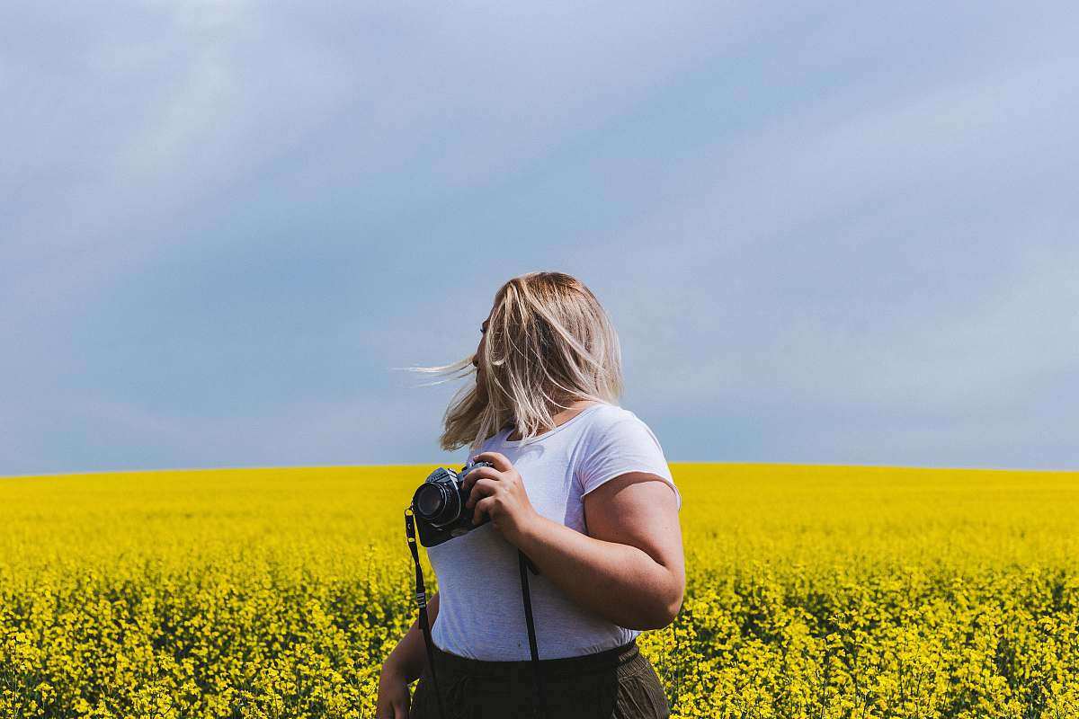 people woman holding DSLR camera standing in front of yellow flower field person