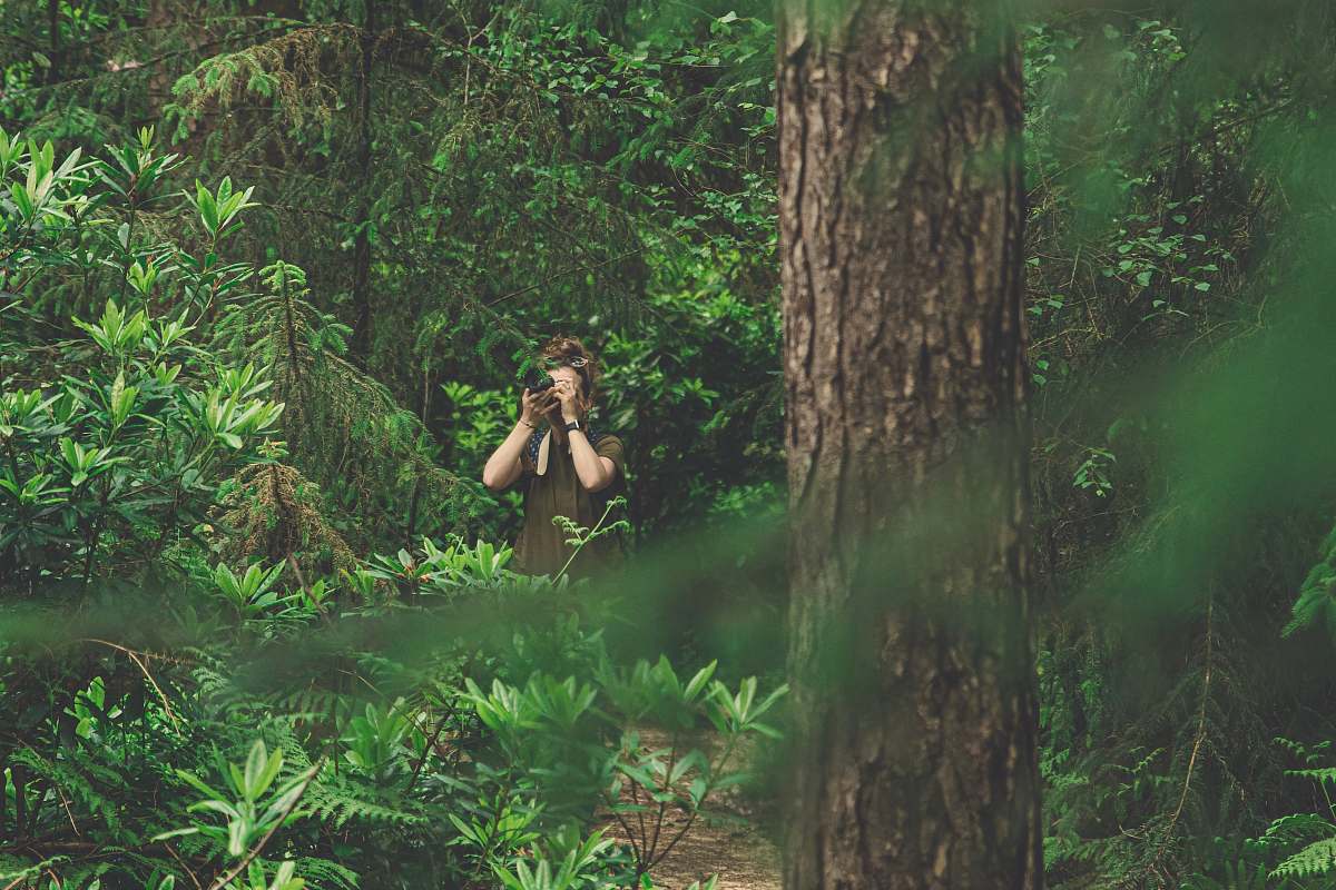 person woman in green dress taking picture in the woods tree