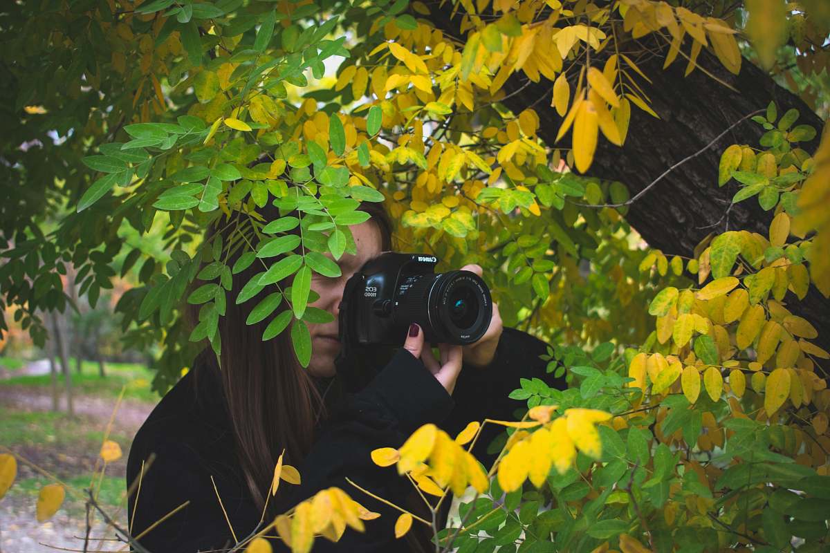 person woman taking photo beside tree camera