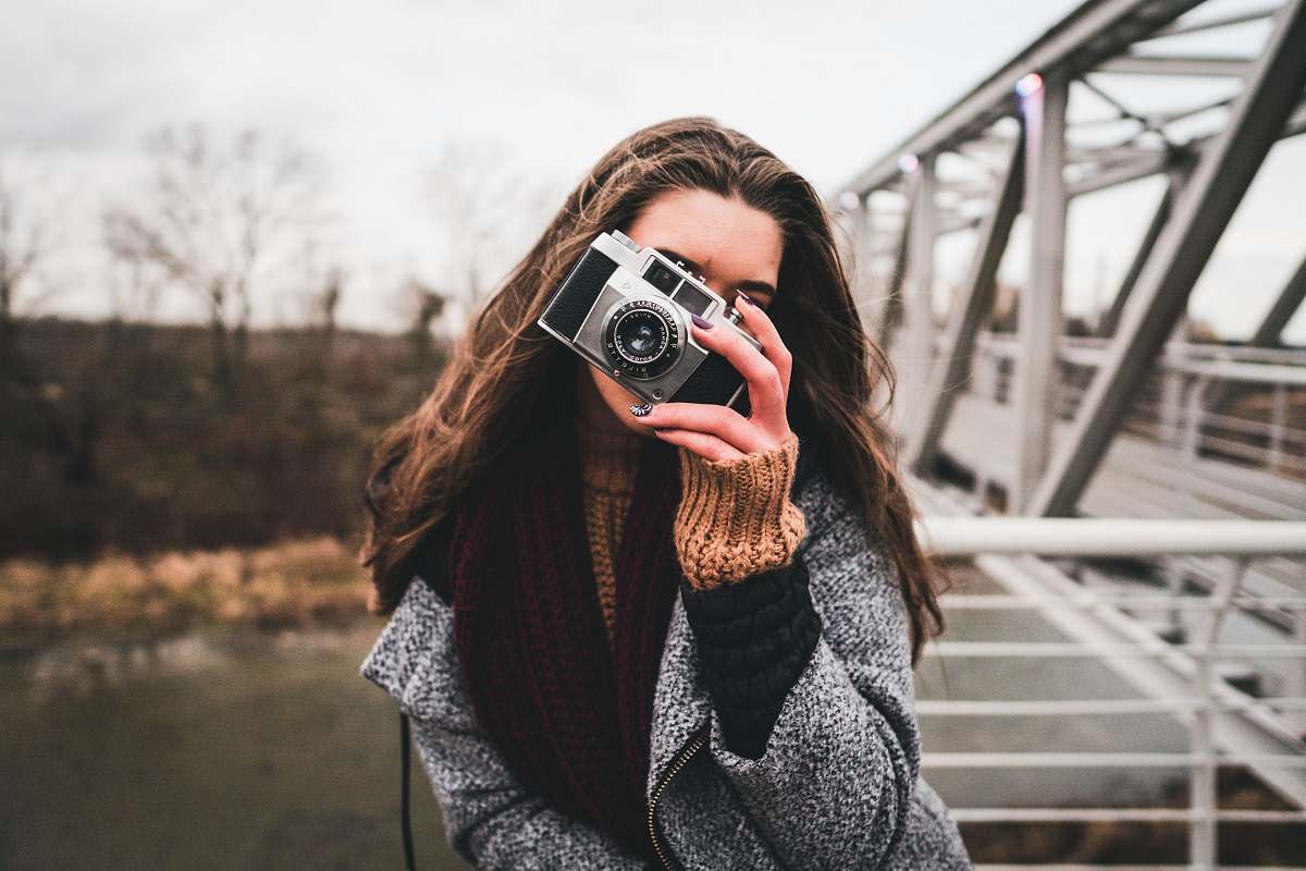 camera woman using camera leaning on handrail near bridge electronics