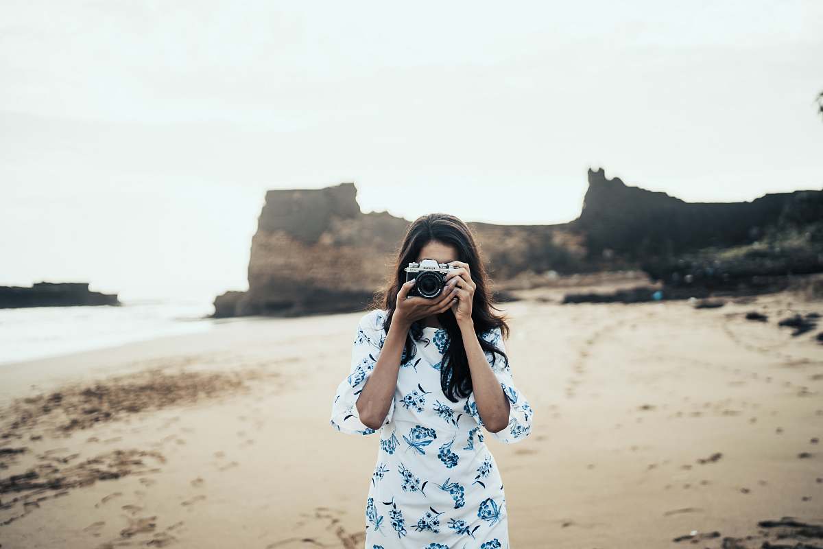 person woman wearing white and blue floral dress holding black and gray camera diu
