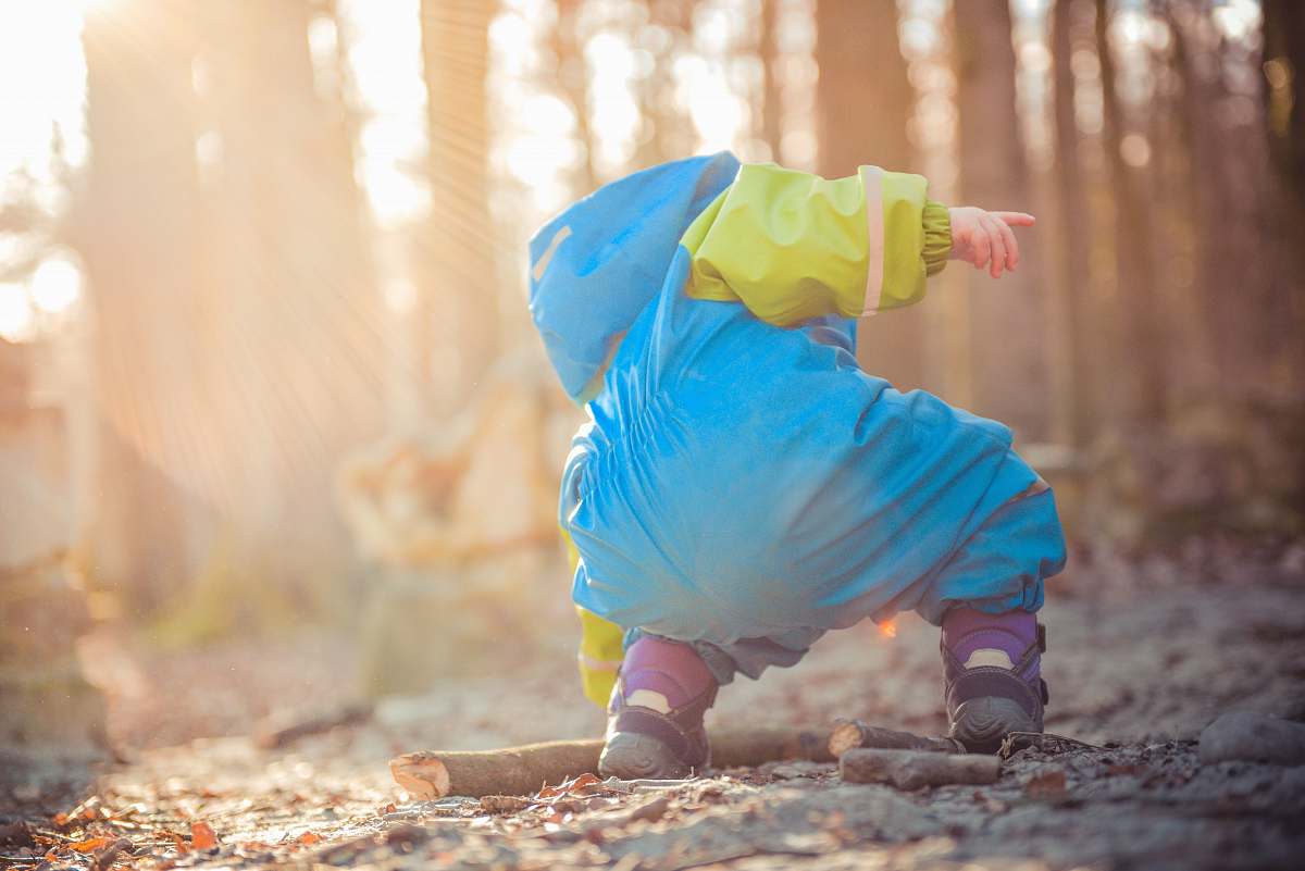 child toddler picking up tree branch forest