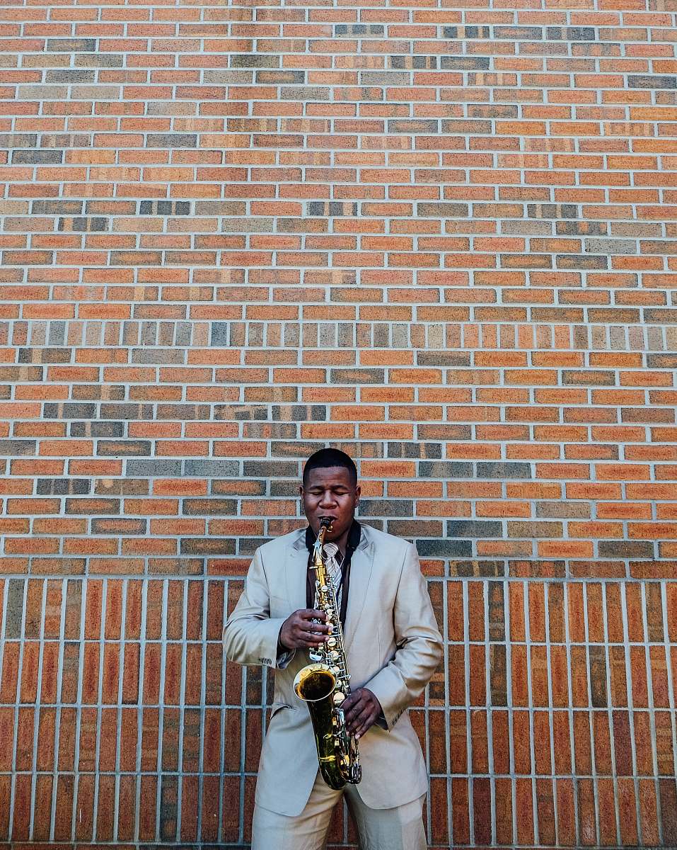 person man playing saxophone near concrete brick people
