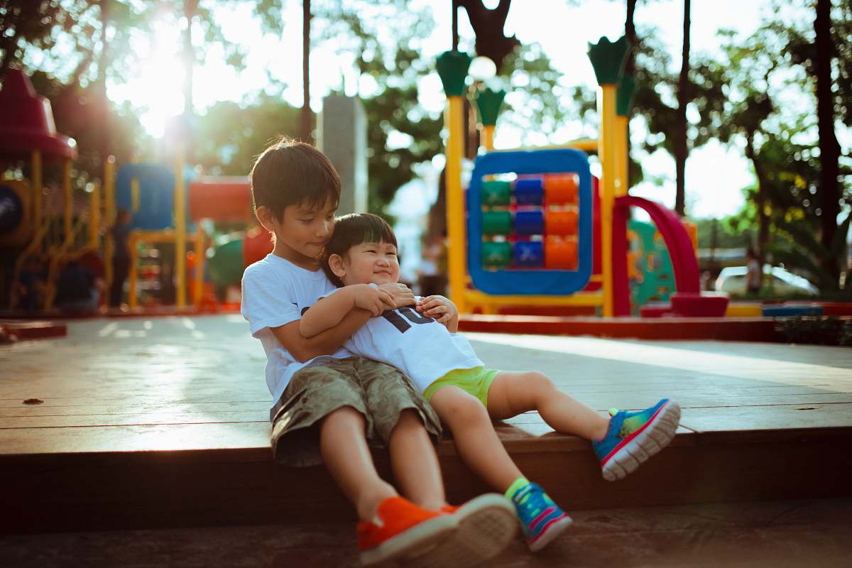 person boy carrying child while sitting on gray concrete platform playground