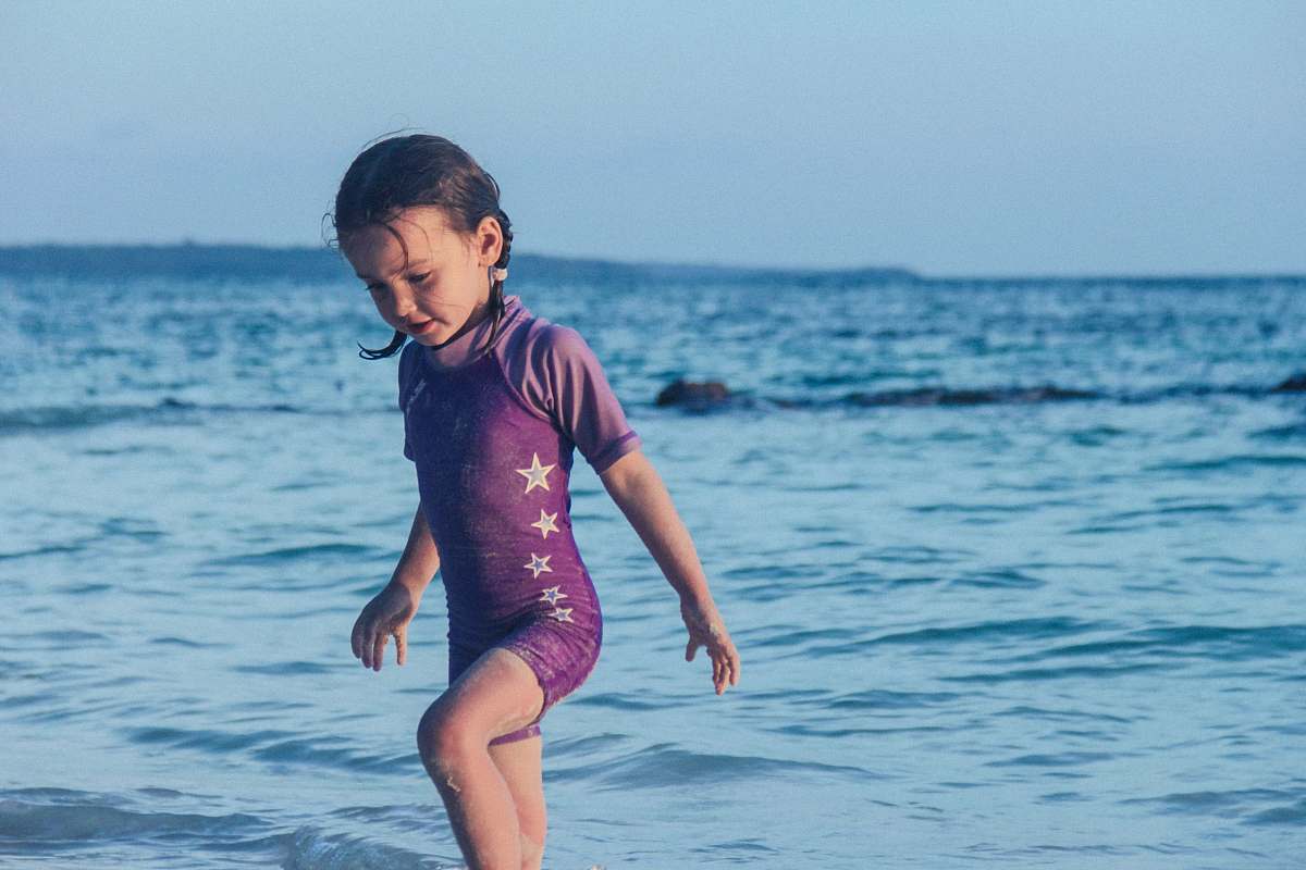 human girl in purple swim wear standing near shore beach