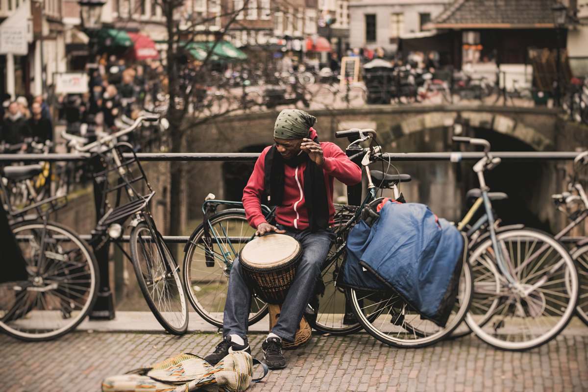 person man in red shirt playing darbuka drum while sitting on gray bike near at deck rail bicycle