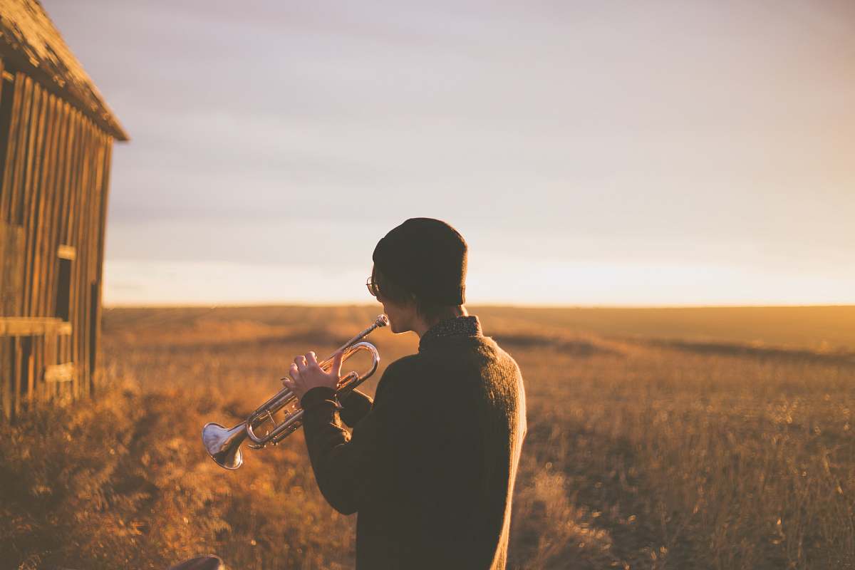 person man playing trumpet outside house on field during daytime music