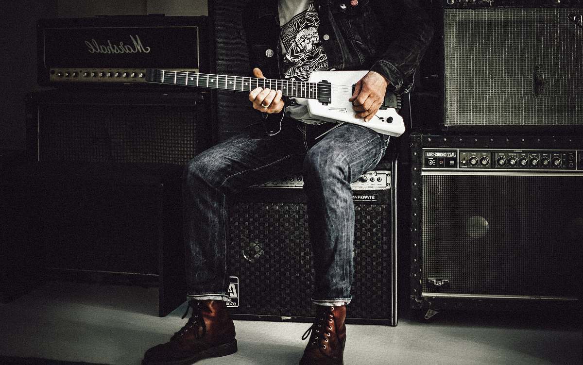 music man wearing blue denim jeans playing white and black electric guitar sitting on black guitar amplifier musician