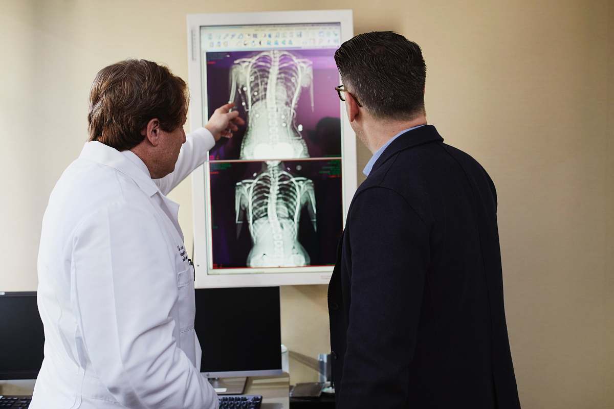 human man in white coat explaining X-Ray results to man in black suit jacket clothing