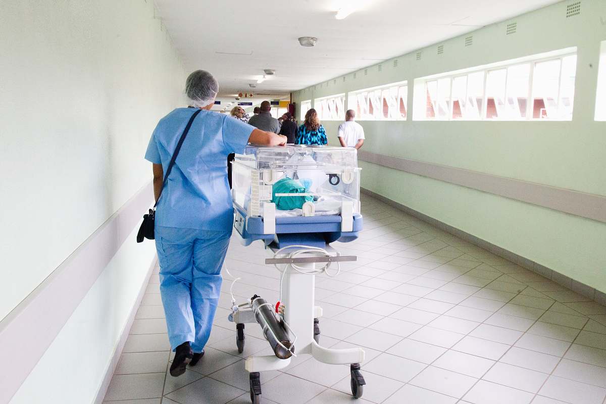 medical person walking on hallway in blue scrub suit near incubator hospital