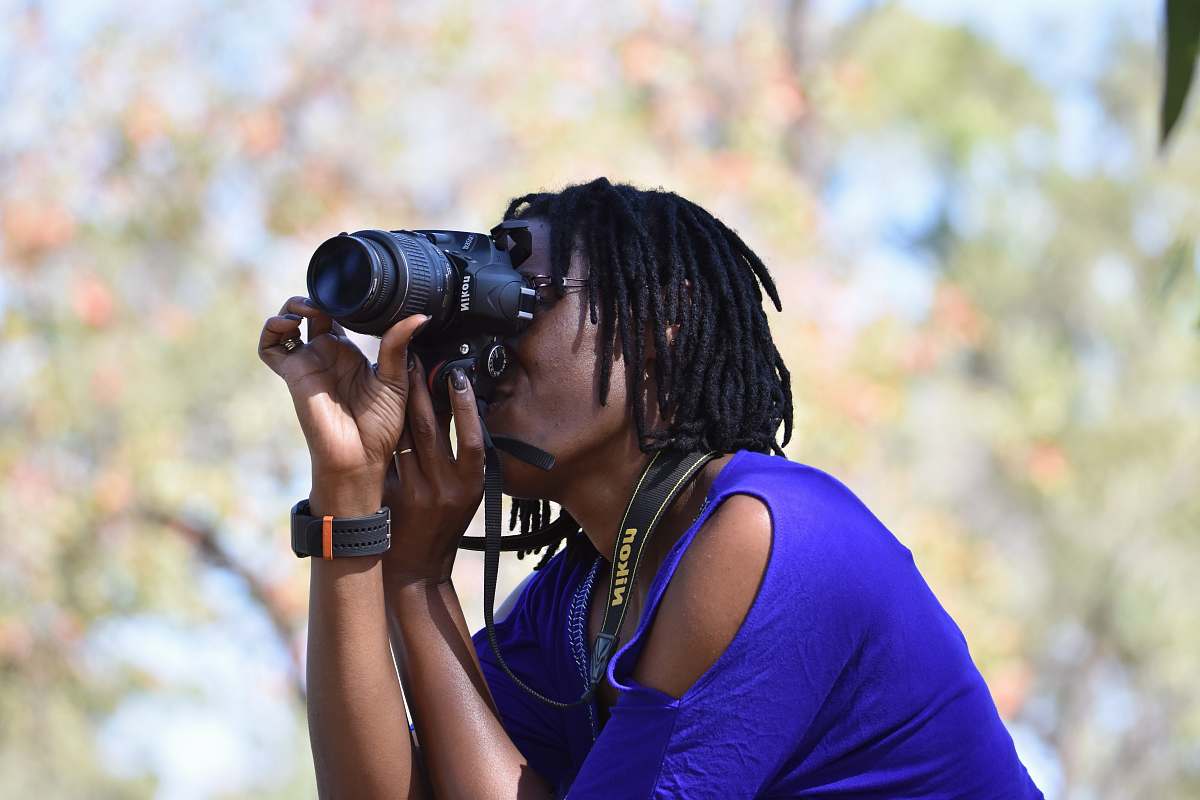 human woman in blue cold-shoulder top taking photo using black DSLR camera photo