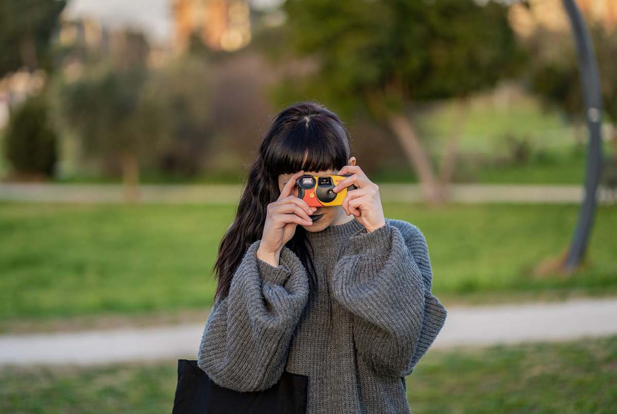 human woman wearing gray knitted sweater holding yellow point-and-shoot camera photo
