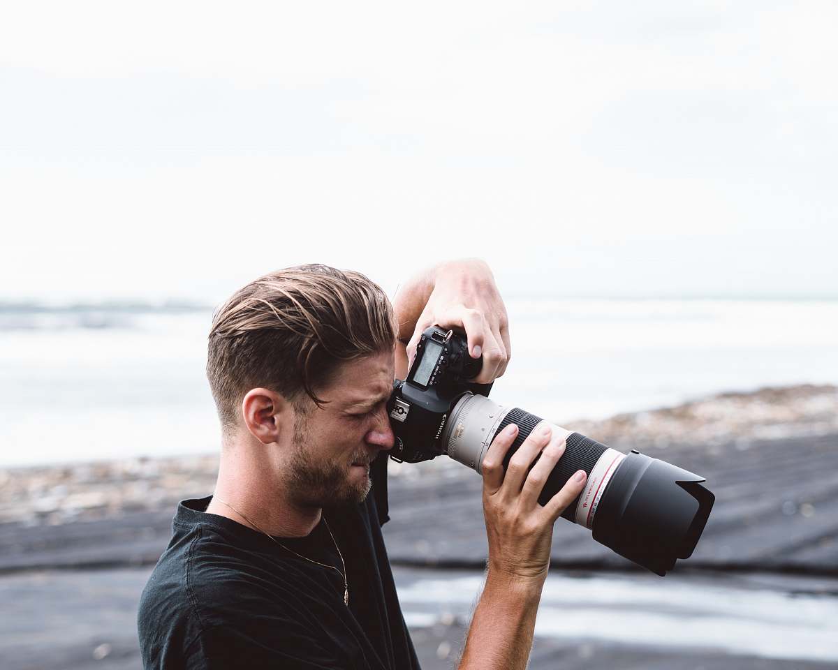 human man holding black bridge camera near sea person