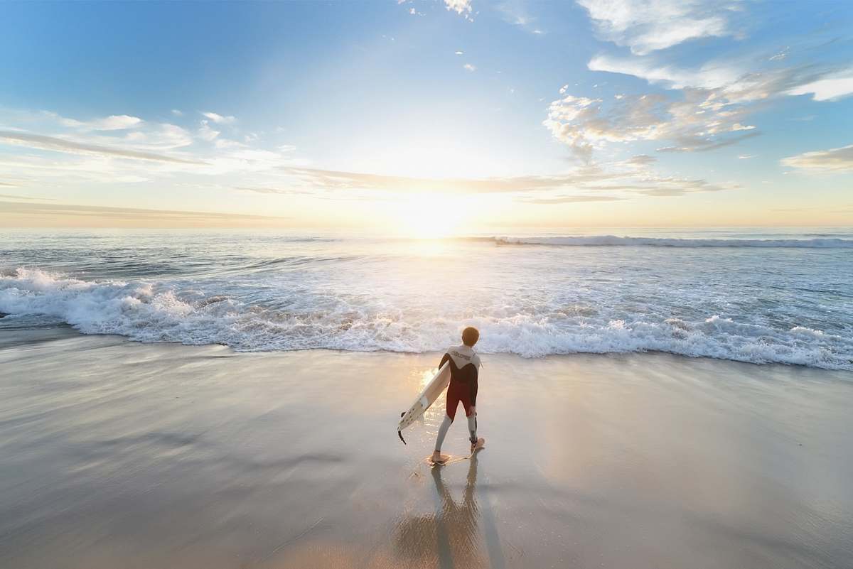 water man holding surfboard walking on shore during daytime ocean