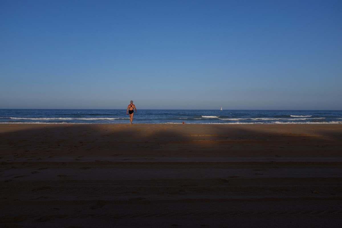 ocean woman in black one-piece swimsuit facing blue wavy ocean under clear blue sky sea