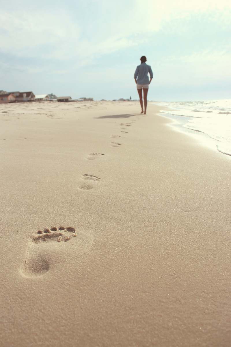 footprint woman wearing blue dress shirt and white short shorts walking on seashore woman