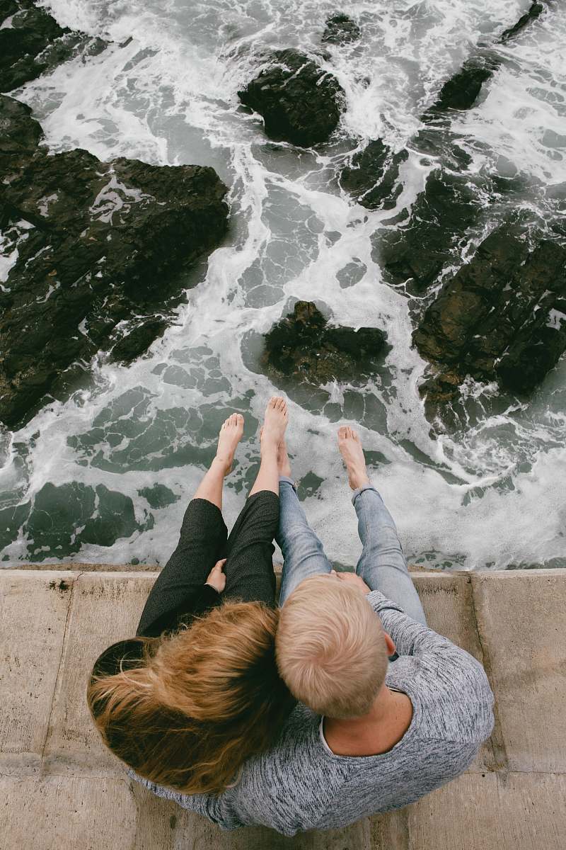 ocean man and woman sitting on cliff near body of water sea