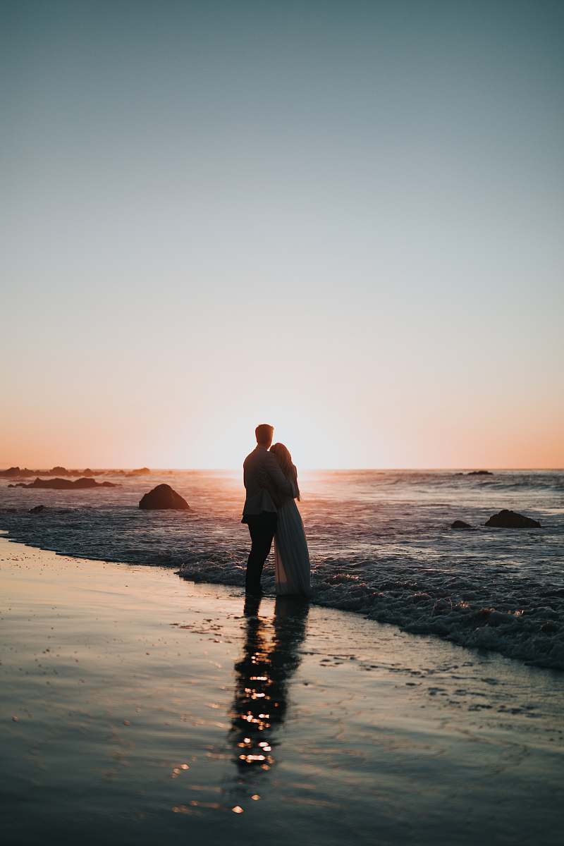 human silhouette photo of couple standing on beach watching sunset person