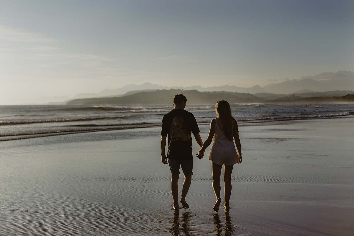 beach man and woman holding hands while walking on body of water coast