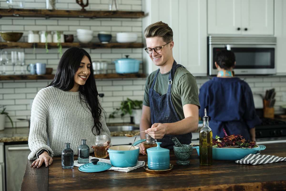person smiling man standing and mixing near woman in kitchen area of the house kitchenware