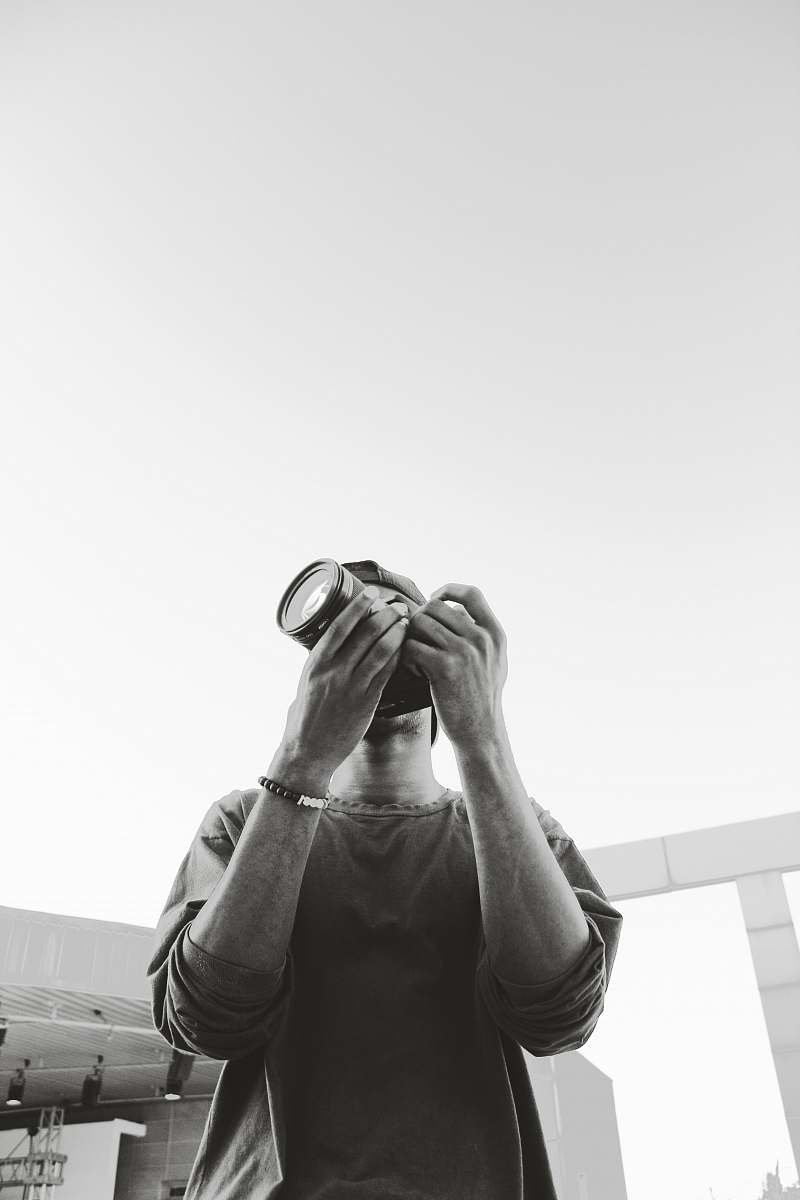person grayscale photography of man standing and holding DSLR camera human
