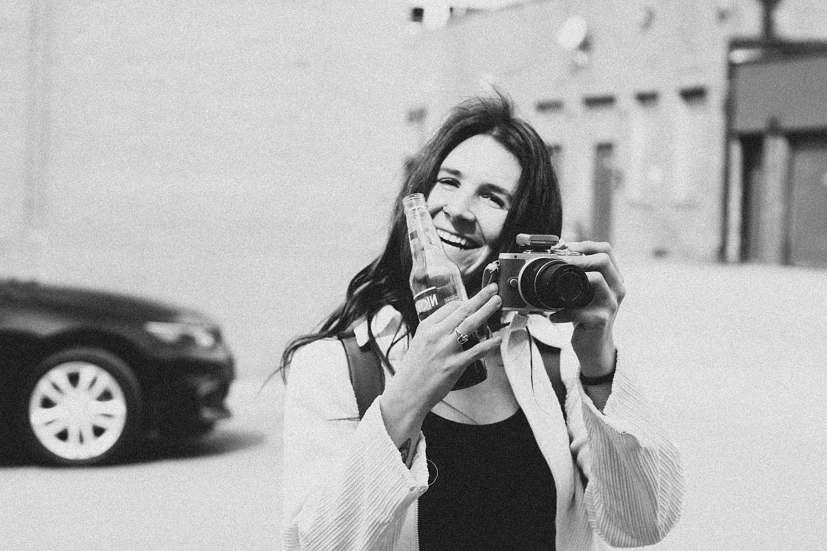 person grayscale photography of person smiling holding bottle and camera black-and-white