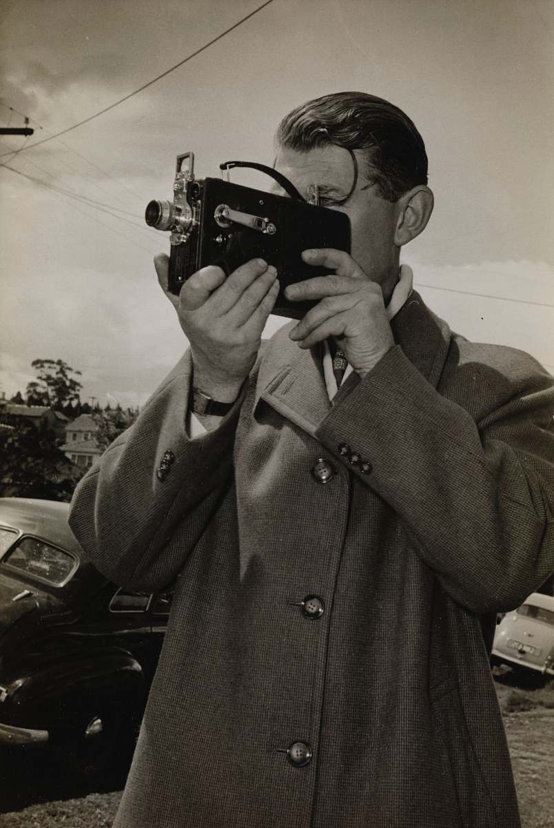 A man confidently holds a sleek black camera, framing the perfect self-portrait in an urban setting. This captivating image captures the essence of modern photography, ideal for blog posts, articles on self-expression, and marketing materials aimed at photography enthusiasts. The subject's focused expression and stylish demeanor highlight the growing trend of personal storytelling through visual art. Perfect for use in both personal and professional projects, this image embodies creativity and self-discovery.