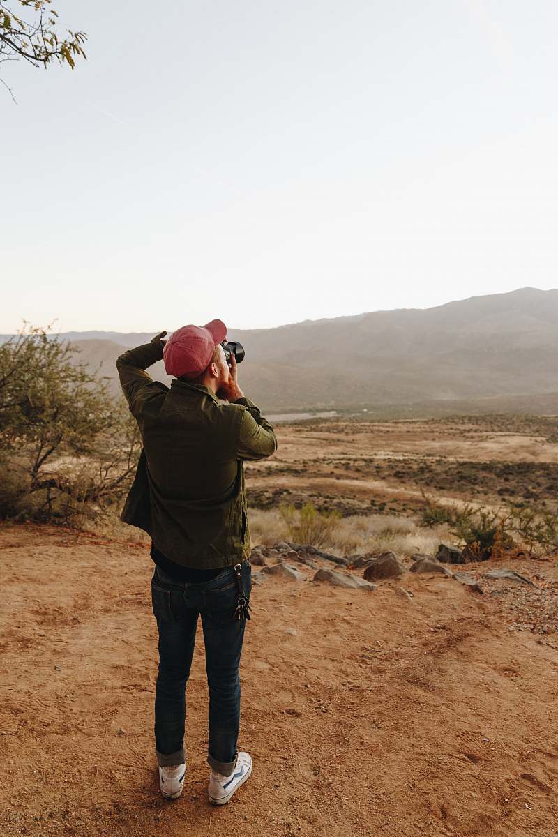 person man standing near cliff using DSLR camera apparel