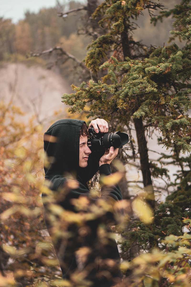 person man taking a photo using black DSLR camera near green-leafed tres photographer