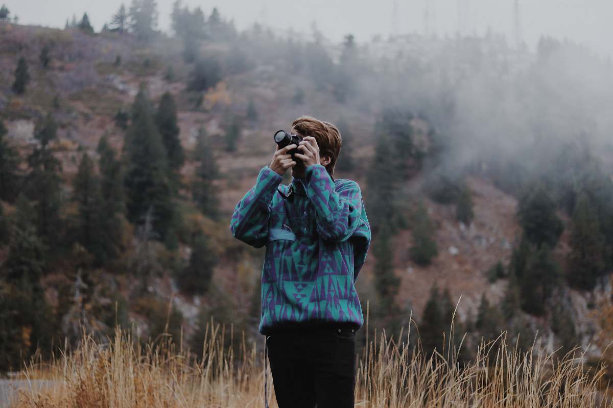 person man using black DSLR camera standing on grassfield photo