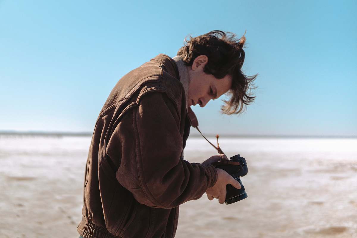 person man wearing brown jacket holding DSLR camera photographer