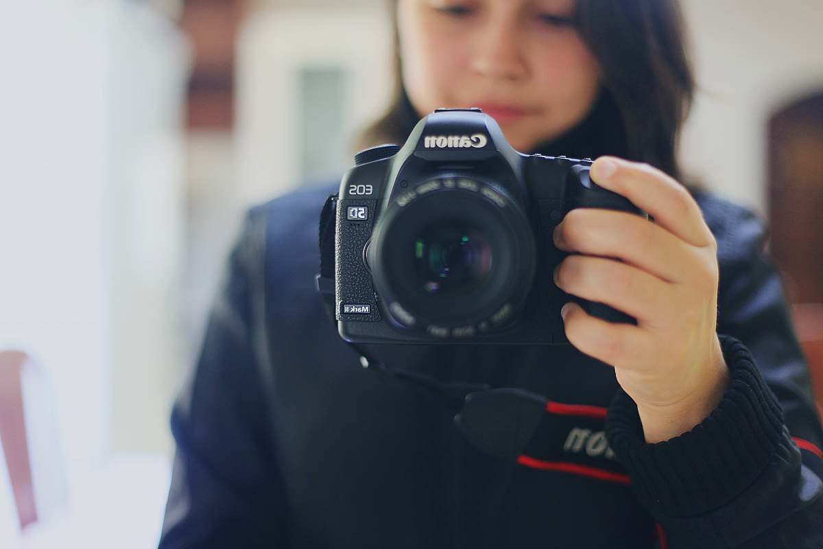 camera person holding black Canon DSLR camera electronics
