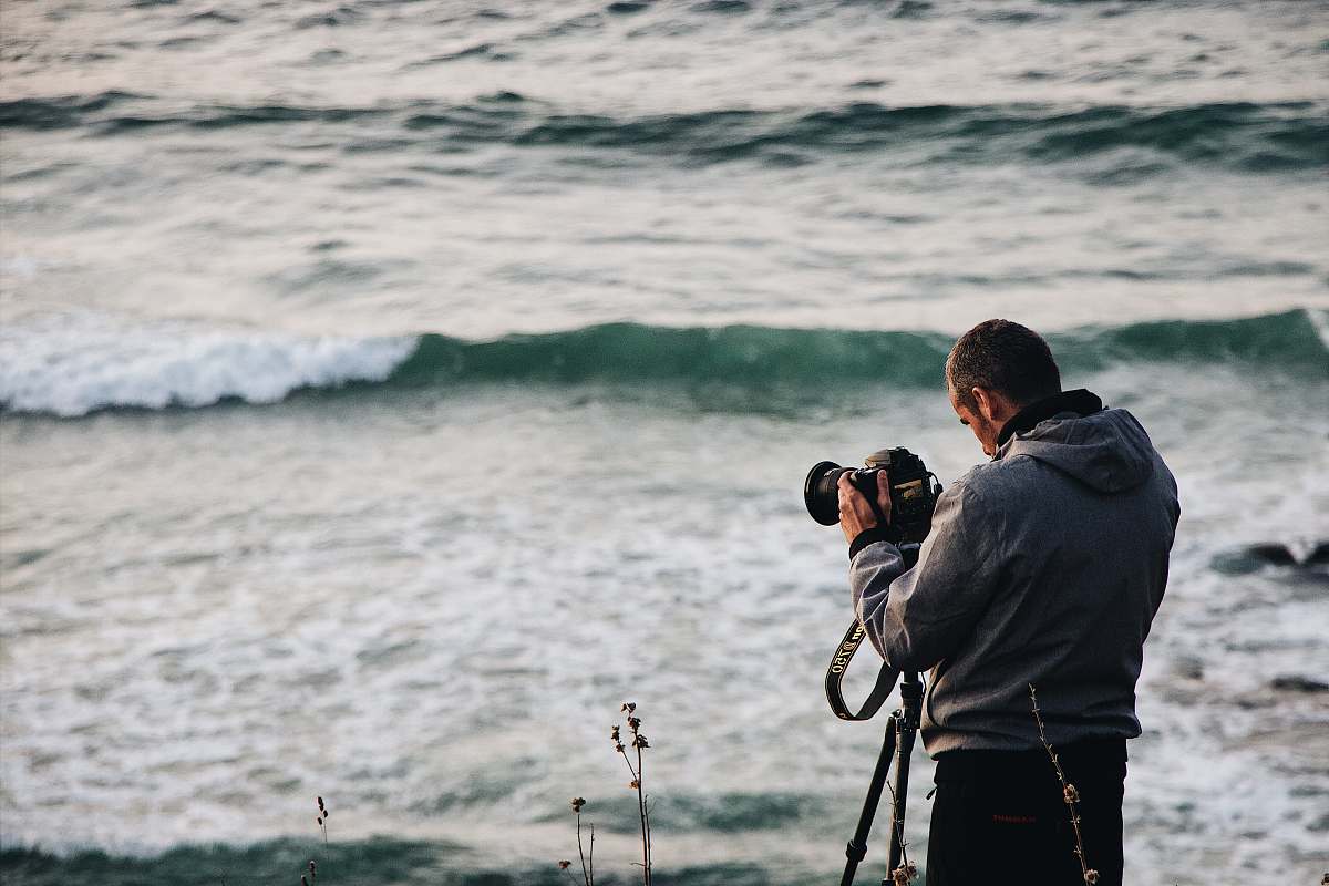 person person holding camera standing beside body of water photo