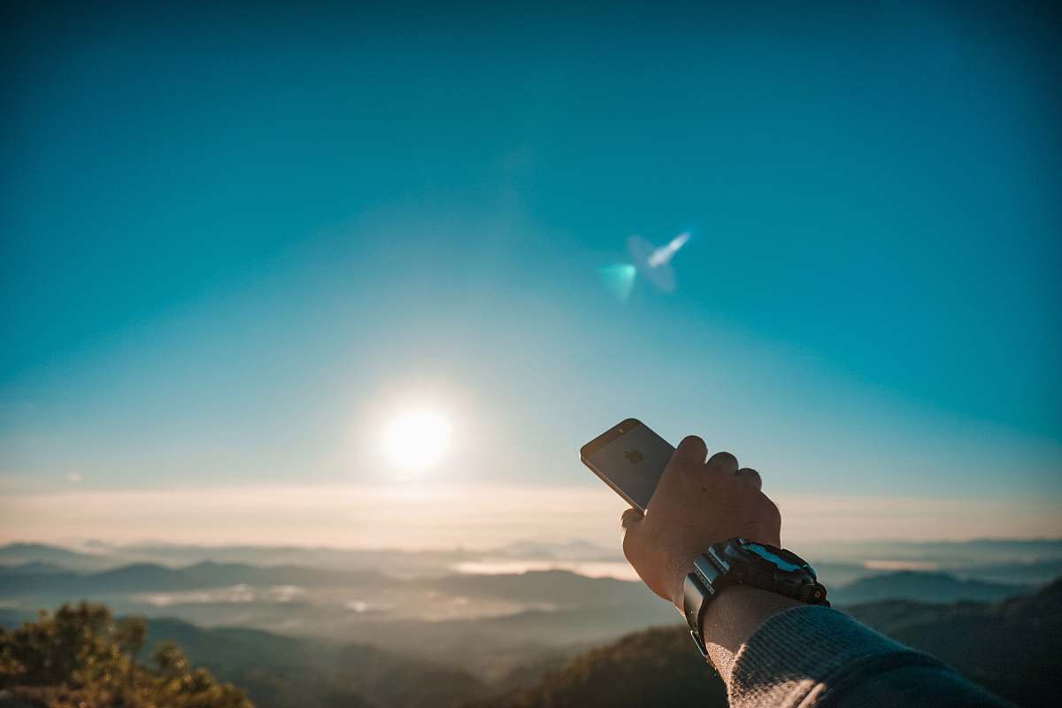 person person holding iPhone overlooking sun and mountains flare