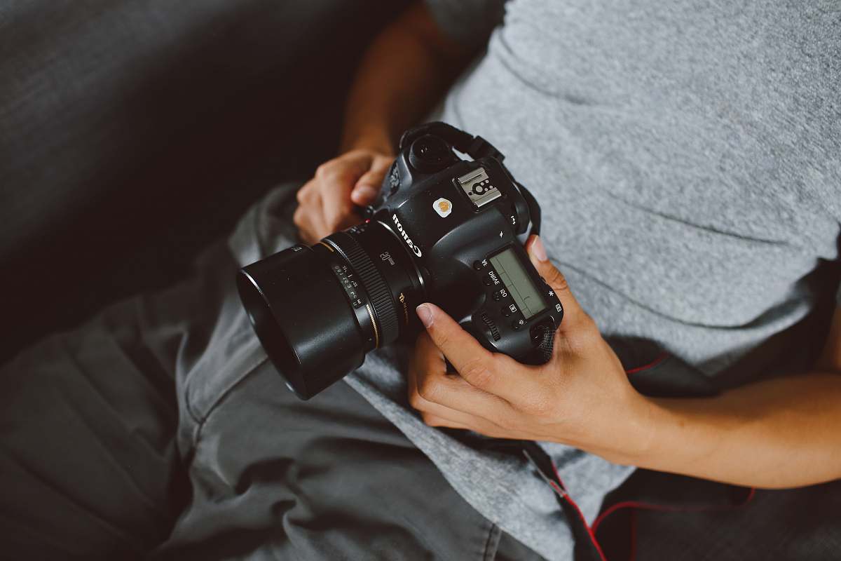 camera person in gray shirt holding black DSLR camera electronics