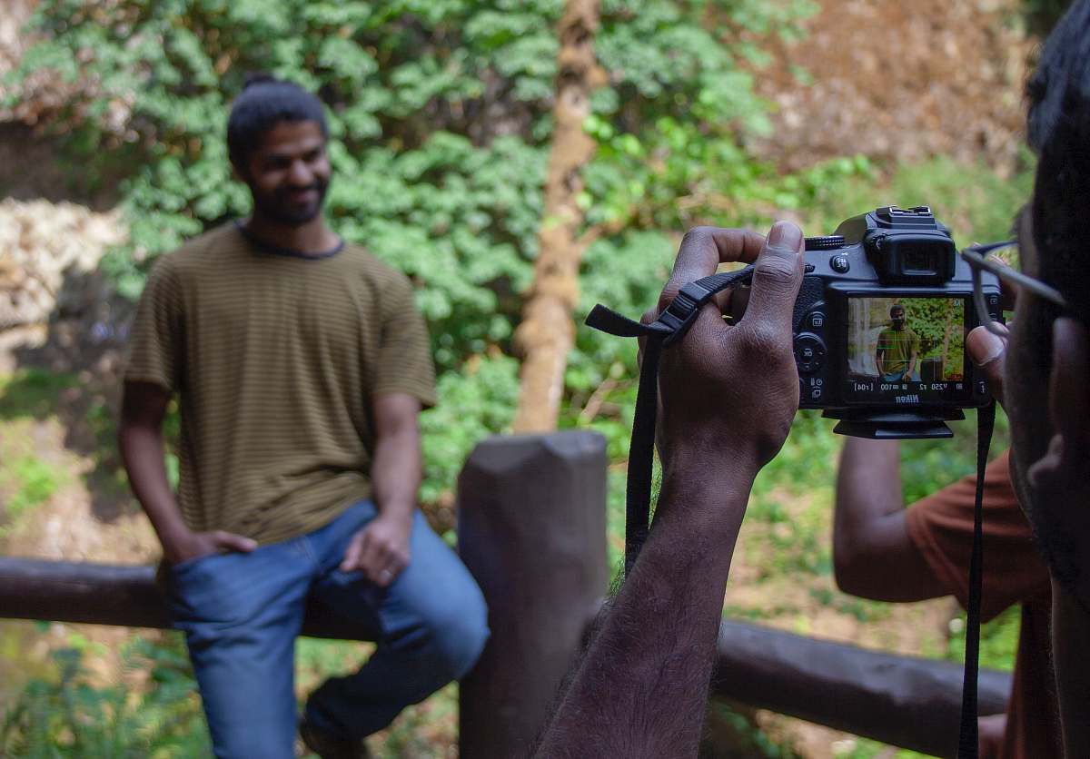 person person taking photo of man in brown shirt sitting on wooden rail camera