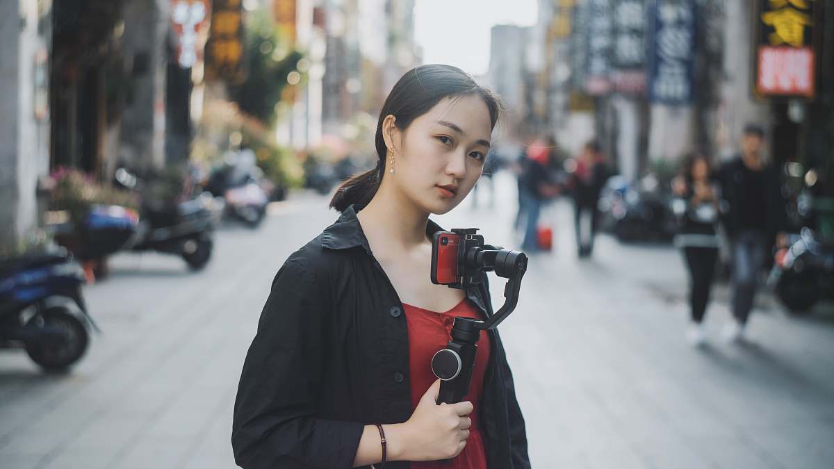 person woman holding gimbal with camera standing in the middle of the road near people and motorcycles machine