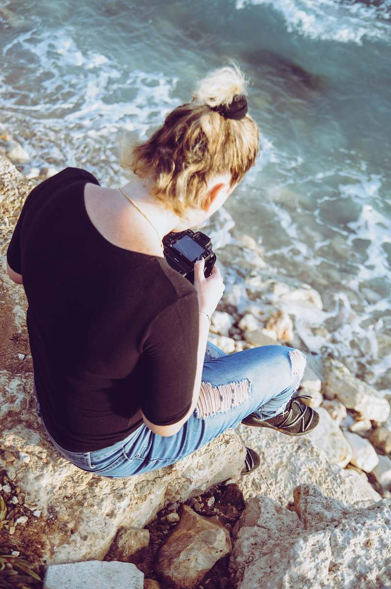 person woman sitting on brown stone holding DSLR camera photo