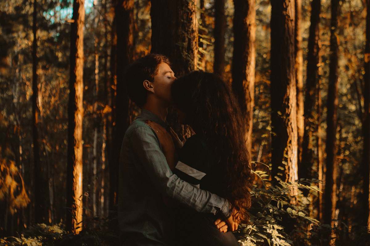 human man kissing woman's forehead in forest tree