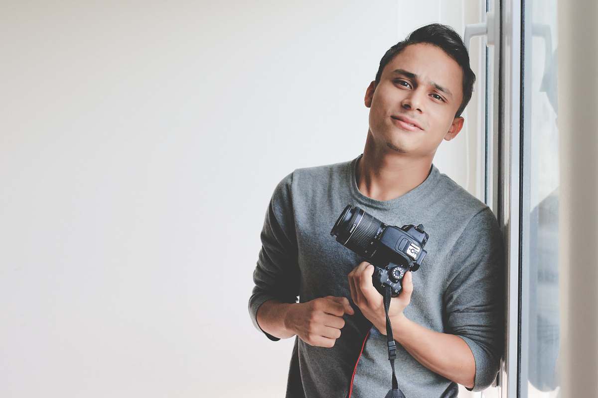 grey man holding DSLR camera leaning on windowpane people