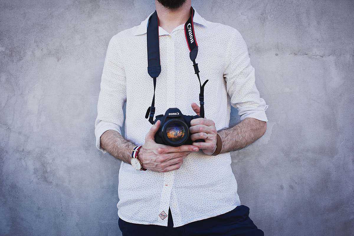 human man in white dress shirt holding Canon DSLR camera lens