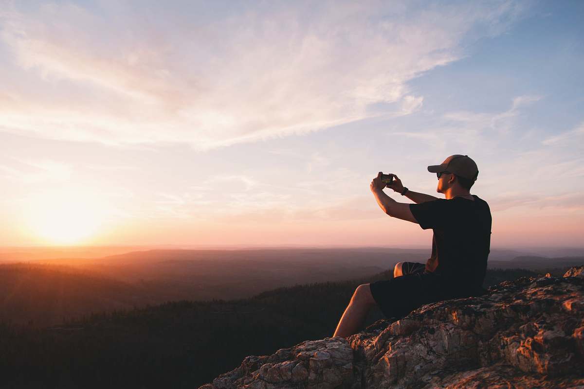 human man sitting on mountain cliff taking picture people