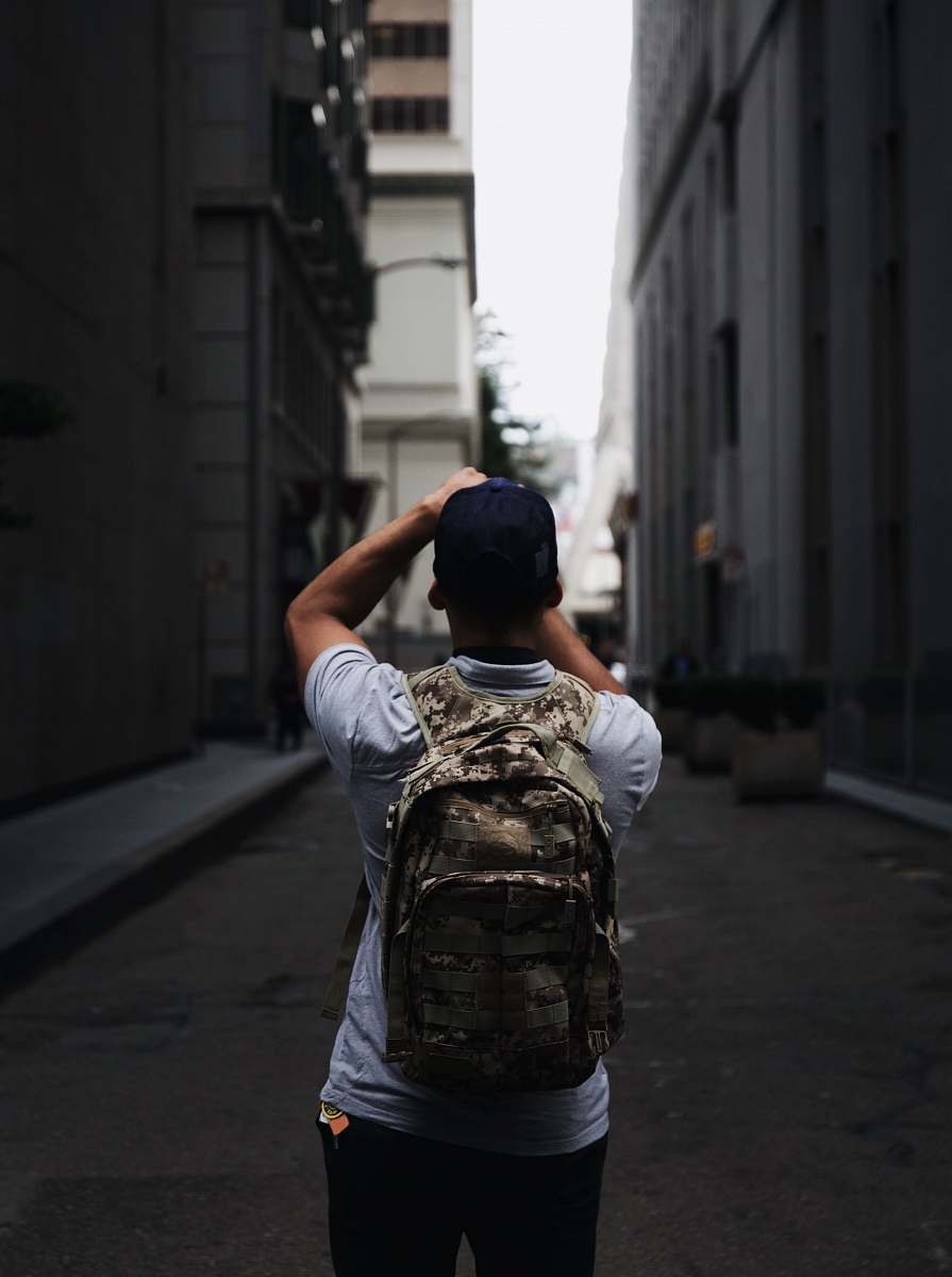 In this captivating urban scene, a lone man stands confidently between two towering buildings, his backpack symbolizing adventure and exploration. The image captures the essence of city life, perfect for travel blogs, lifestyle articles, or promotional materials for outdoor gear. Ideal for depicting themes of adventure, urban exploration, and the modern wanderer, this photograph offers a dynamic view of an individual navigating the vibrant streets of a city.