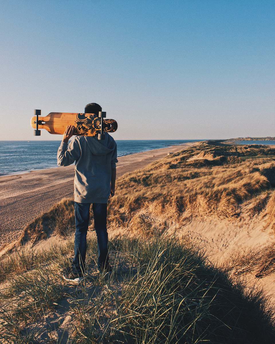 human person holding a skateboard in a hill near body of water during daytime photo