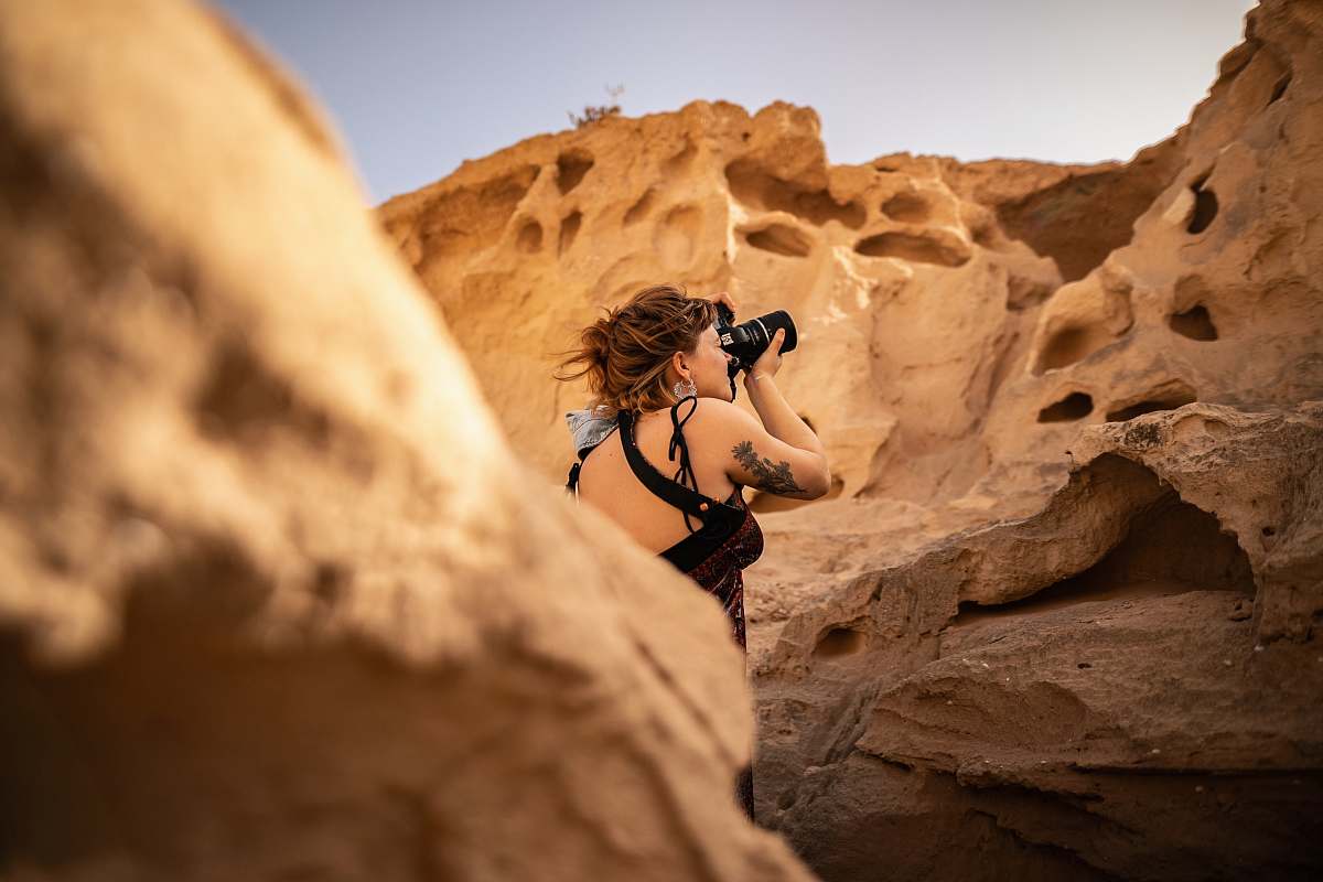 human photography of woman standing near rock formation while taking photo during daytime nature