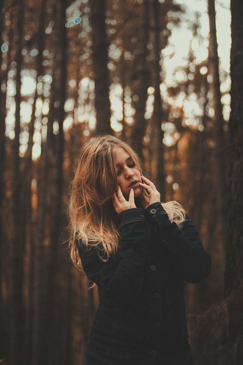 people portrait photography of woman wearing black coat surrounded by forest trees during daytime female