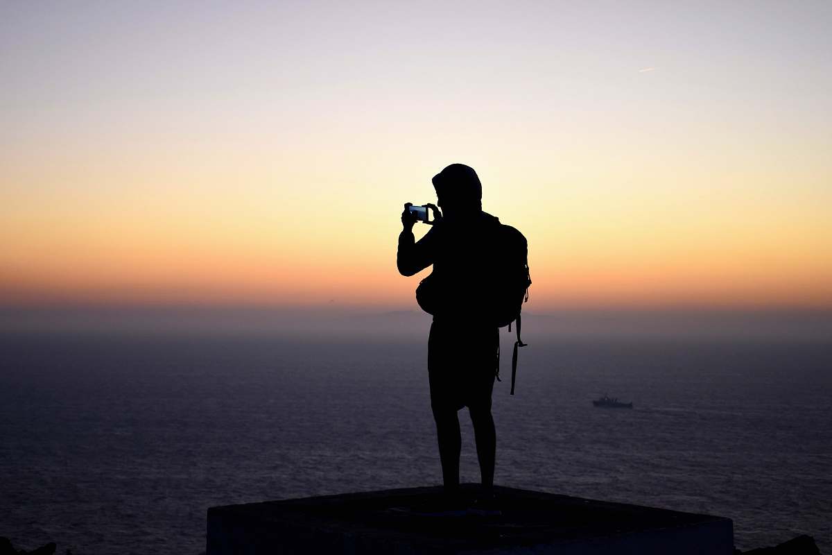 human silhouette photography of person standing in front of calm body of water during golden hour photography
