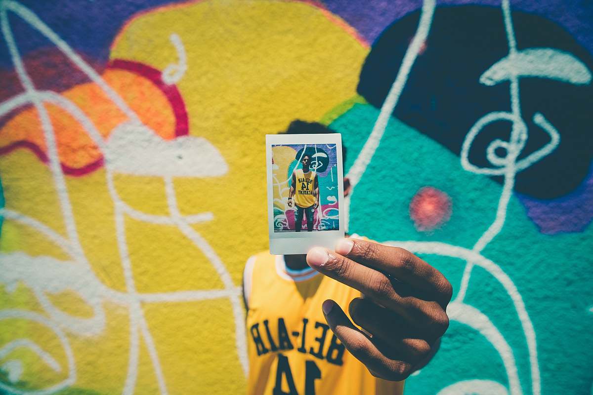 hand person holding printed photo of him with graffiti as background graffiti
